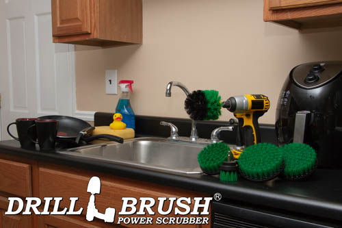 The Drillbrush 542O Medium Green Kitchen Brush Kit in a cordless drill sitting on a kitchen counter in front of a sink, coffeemaker, and dishes.