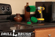 The Drillbrush 42J Medium Green Kitchen Brush Kit in a cordless drill sitting on a counter next to a stove in front of a microwave and decorative vases.