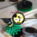 Action shots of a Medium Green Original brush cleaning around a burner and a Medium Green 4 inch Drillbrush cleaning wine stains on a stovetop.
