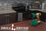 The Drillbrush 52O Medium Green Kitchen Brush Kit in a cordless drill sitting on a dinner table in front of kitchen counters, a stove, a toaster, and a microwave.