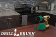 The Drillbrush 52O Medium Green Kitchen Brush Kit in a cordless drill sitting on a dinner table in front of kitchen counters, a stove, a toaster, and a microwave.