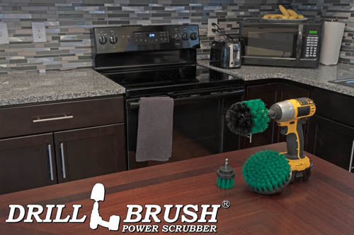 The Drillbrush 52O Medium Green Kitchen Brush Kit in a cordless drill sitting on a dinner table in front of kitchen counters, a stove, a toaster, and a microwave.