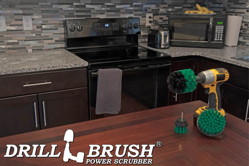 The Drillbrush 42O Medium Green Kitchen Brush Kit in a cordless drill sitting on a dinner table in front of kitchen counters, a stove, a toaster, and a microwave.