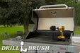 The Drillbrush 42OS-2L Ultra Stiff Black Grill & Industrial Brush Kit in a cordless drill sitting on an open grill in front of a grassy backyard.