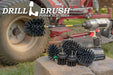 The Drillbrush 542OMS-2L-7X Ultra Stiff Black Grill & Industrial Brush Kit in a cordless drill sitting on stone bricks in front of a ride-on lawnmower.