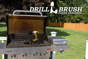 The Drillbrush 542OMS-2L Ultra Stiff Black Grill & Industrial Brush Kit in a cordless drill sitting on an open grill in front of a grassy backyard.