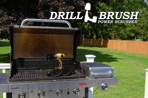 The Drillbrush 5542O Ultra Stiff Black Grill & Industrial Brush Kit in a cordless drill sitting on an open grill in front of a grassy backyard.