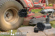 The Drillbrush 42O-5X Ultra Stiff Black Grill & Industrial Brush Kit in a cordless drill sitting on a stone block in front of a ride-on lawnmower.