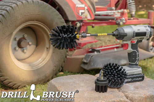 The Drillbrush 42O-5X Ultra Stiff Black Grill & Industrial Brush Kit in a cordless drill sitting on a stone block in front of a ride-on lawnmower.