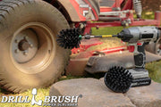 The Drillbrush 4M-5X Ultra Stiff Black Brush Kit in a cordless drill sitting on stone bricks in front of a ride-on lawnmower.