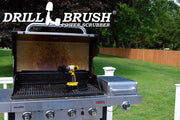 The Drillbrush 4M Ultra Stiff Black Grill & Industrial Brush Kit in a cordless drill sitting on an open grill in front of a grassy backyard.