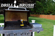 The Drillbrush 4M Ultra Stiff Black Grill & Industrial Brush Kit in a cordless drill sitting on an open grill in front of a grassy backyard.