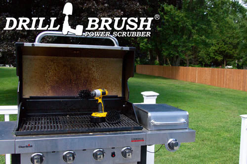 The Drillbrush 4M Ultra Stiff Black Grill & Industrial Brush Kit in a cordless drill sitting on an open grill in front of a grassy backyard.