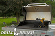 The Drillbrush 52O Ultra Stiff Black Grill & Industrial Brush Kit in a cordless drill sitting on an open grill in front of a grassy backyard.