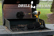 The Drillbrush 542O-7X Ultra Stiff Black Grill & Industrial Brush Kit in a cordless drill sitting on an open grill in front of a grassy backyard.
