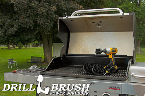 The Drillbrush 542O Ultra Stiff Black Grill & Industrial Brush Kit in a cordless drill sitting on an open grill in front of a grassy backyard.