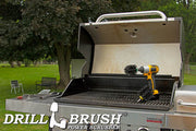 The Drillbrush MO Ultra Stiff Black Grill & Industrial Brush Kit in a cordless drill sitting on an open grill in front of a grassy backyard.
