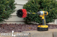 Drillbrush Original Stiff Red Outdoor & Patio Brush in a 5 inch extension on a brick planter in front of a rock garden and bushes.