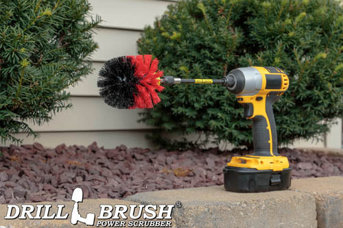 Drillbrush Original Stiff Red Outdoor & Patio Brush in a 5 inch extension on a brick planter in front of a rock garden and bushes.