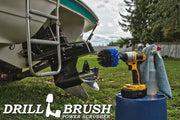 Drillbrush Original Medium Blue Marine & Pool Brush in a cordless drill on a bucket next to a spray bottle and rag in front of a boat on a trailer in a backyard.