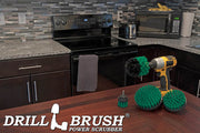 The Drillbrush 542O Medium Green Kitchen Brush Kit in a cordless drill sitting on a dinner table in front of kitchen counters, a stove, a toaster, and a microwave.
