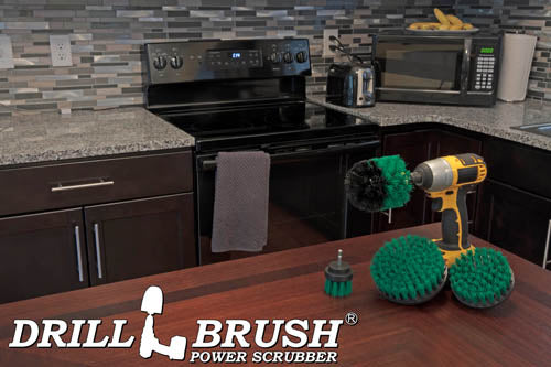 The Drillbrush 542O Medium Green Kitchen Brush Kit in a cordless drill sitting on a dinner table in front of kitchen counters, a stove, a toaster, and a microwave.