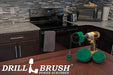 The Drillbrush 542O Medium Green Kitchen Brush Kit in a cordless drill sitting on a dinner table in front of kitchen counters, a stove, a toaster, and a microwave.