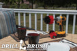 The Drillbrush MO Red Stiff Outdoor & Patio Brush Kit in a cordless drill sitting on a deck table set with forks, mugs, and paper plates in from of a grassy backyard.