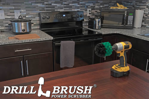 Drillbrush Original Medium Green Kitchen Brush on a table in front of a kitchen counter, stove, microwave, and other appliances.