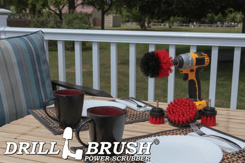 The Drillbrush 42OS-2L Red Stiff Outdoor & Patio Brush Kit in a cordless drill sitting on a deck table set with forks, mugs, and paper plates in from of a grassy backyard.