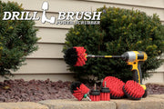 The Drillbrush 542OMS-2L-7X Red Stiff Outdoor & Patio Brush Kit in a cordless drill sitting on a stone planter in front of a rock garden and some shrubs.