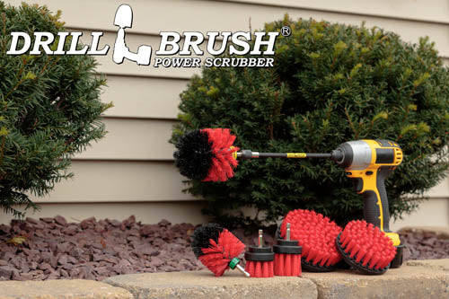 The Drillbrush 542OMS-2L-7X Red Stiff Outdoor & Patio Brush Kit in a cordless drill sitting on a stone planter in front of a rock garden and some shrubs.