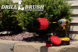 The Drillbrush 42J-5X Red Stiff Outdoor & Patio Brush Kit in a cordless drill sitting on brick planter in front of some shrubs.