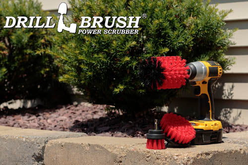 The Drillbrush 42J Red Stiff Outdoor & Patio Brush Kit in a cordless drill sitting on a brick planter in front of some shrubs.