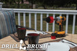 The Drillbrush MS-2L Red Stiff Outdoor & Patio Brush Kit in a cordless drill sitting on a deck table set with forks, mugs, and paper plates in from of a grassy backyard.