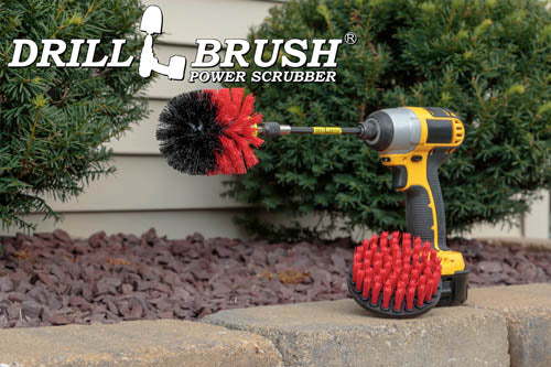 The Drillbrush 4O-5X Red Stiff Outdoor & Patio Brush Kit in a cordless drill sitting on a brick planter in front of a rock garden and some shrubs.