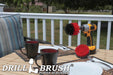 The Drillbrush 4O Red Stiff Outdoor & Patio Brush Kit in a cordless drill sitting on a deck table set with forks, mugs, and paper plates in from of a grassy backyard.