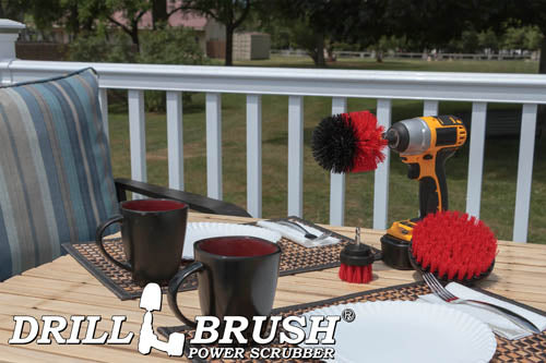 The Drillbrush 52O Red Stiff Outdoor & Patio Brush Kit in a cordless drill sitting on a deck table set with forks, mugs, and paper plates in from of a grassy backyard.