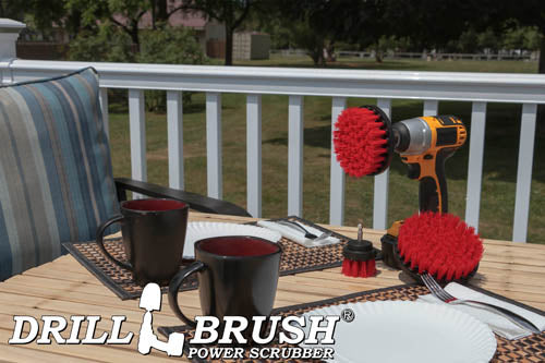 The Drillbrush 542 Red Stiff Outdoor & Patio Brush Kit in a cordless drill sitting on a deck table set with forks, mugs, and paper plates in from of a grassy backyard.