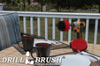 The Drillbrush 5O Red Stiff Outdoor & Patio Brush Kit in a cordless drill sitting on a deck table set with forks, mugs, and paper plates in from of a grassy backyard.