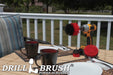 The Drillbrush 42O Red Stiff Outdoor & Patio Brush Kit in a cordless drill sitting on a deck table set with forks, mugs, and paper plates in from of a grassy backyard.