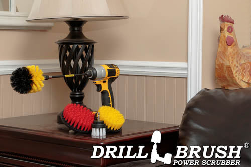 The Drillbrush 542O-7X Variety Brush Kit in a cordless drill sitting on a wooden side table in front of a lamp next to a leather sofa.