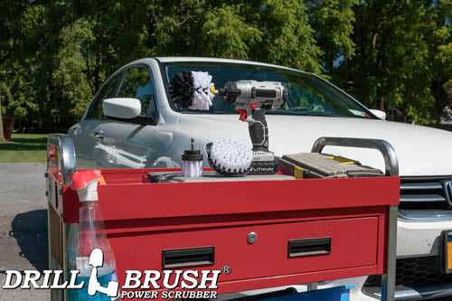 The Drillbrush 4OS-2L Soft White Home & Auto Brush Kit in a cordless drill sitting on a tool cart in front of a white sedan.