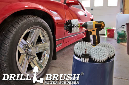 The Drillbrush 5542O Soft White Home & Auto Brush Kit in a cordless drill sitting on a bucket next to a spray bottle and a rag in front of a red sports car.