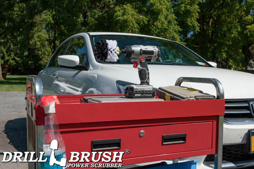 Drillbrush Original Soft White Home & Auto Brush in a cordless drill on a tool cart in front of a white sedan.