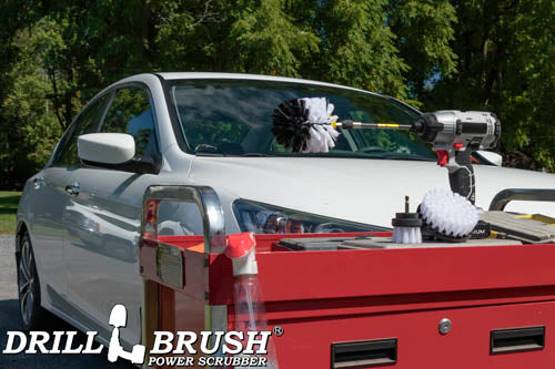 The Drillbrush 42O-5X Soft White Home & Auto Brush Kit in a cordless drill sitting on a tool cart in front of a white sedan.