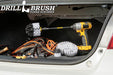 The Drillbrush 542O-7X Soft White Home & Auto Brush Kit in a cordless drill sitting in an opened car trunk in front of jumper cables and auto parts.