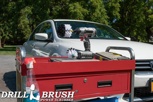 The Drillbrush MO Soft White Home & Auto Brush Kit in a cordless drill sitting on a tool cart in front of a white sedan.
