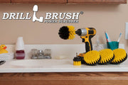The Drillbrush 5542O Medium Yellow Bathroom Brush Kit in a cordless drill sitting on a bathroom counter next to a sink and toiletries.