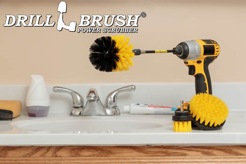 The Drillbrush 42O-5X Medium Yellow Bathroom Brush Kit in a cordless drill sitting on a bathroom counter next to a sink and toiletries.